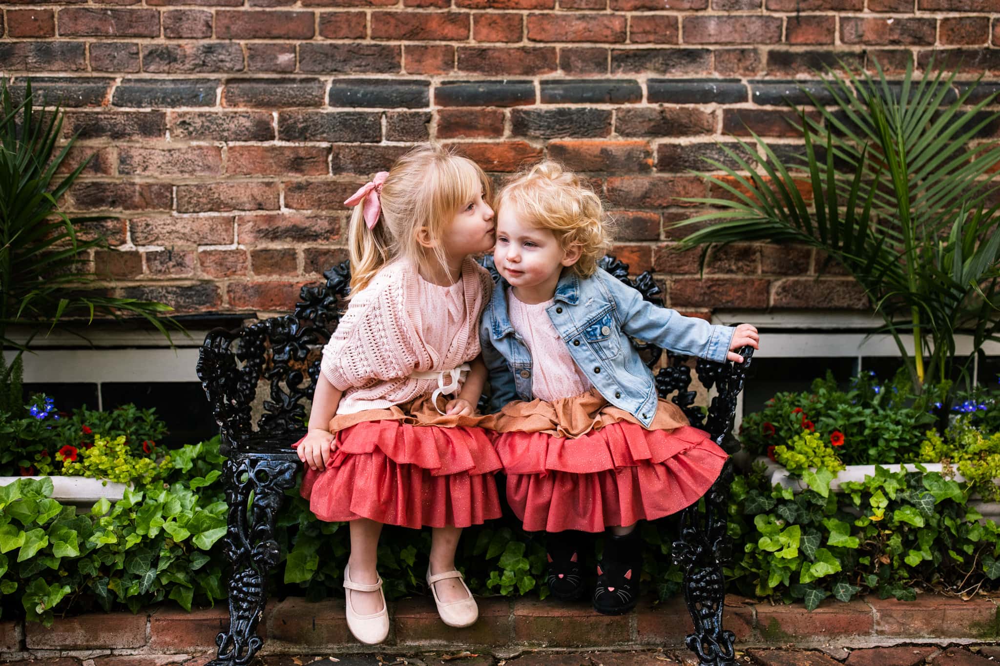 two sisters in matching dresses sit on bench together