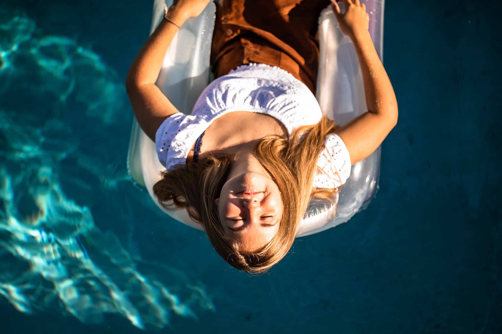 senior girl floats on raft in pool, angle is from above