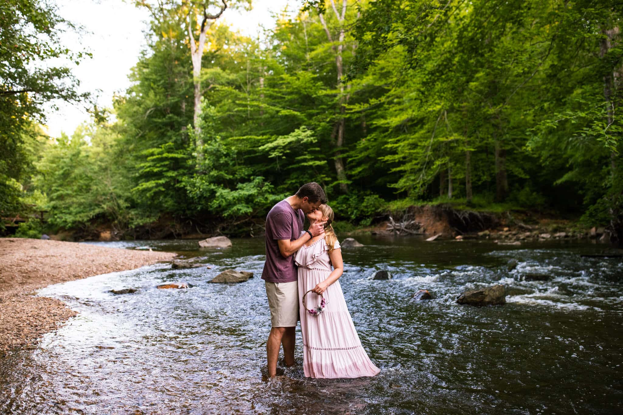 husband and wife stand in creek and kiss