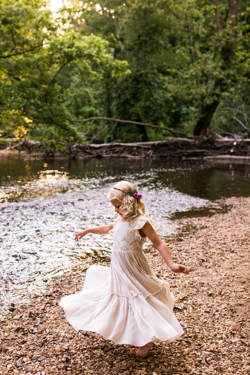 girl spinning in white dress along creek bed