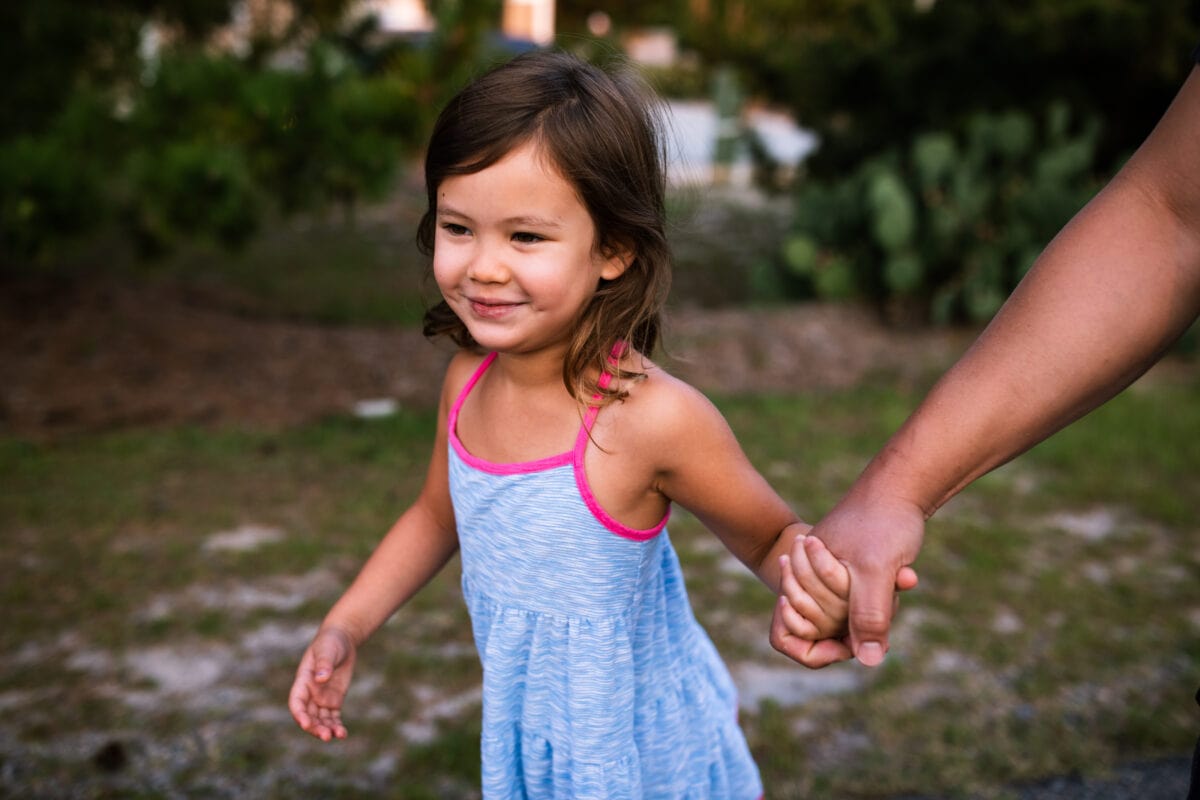 young daughter holds dads hand while smiling
