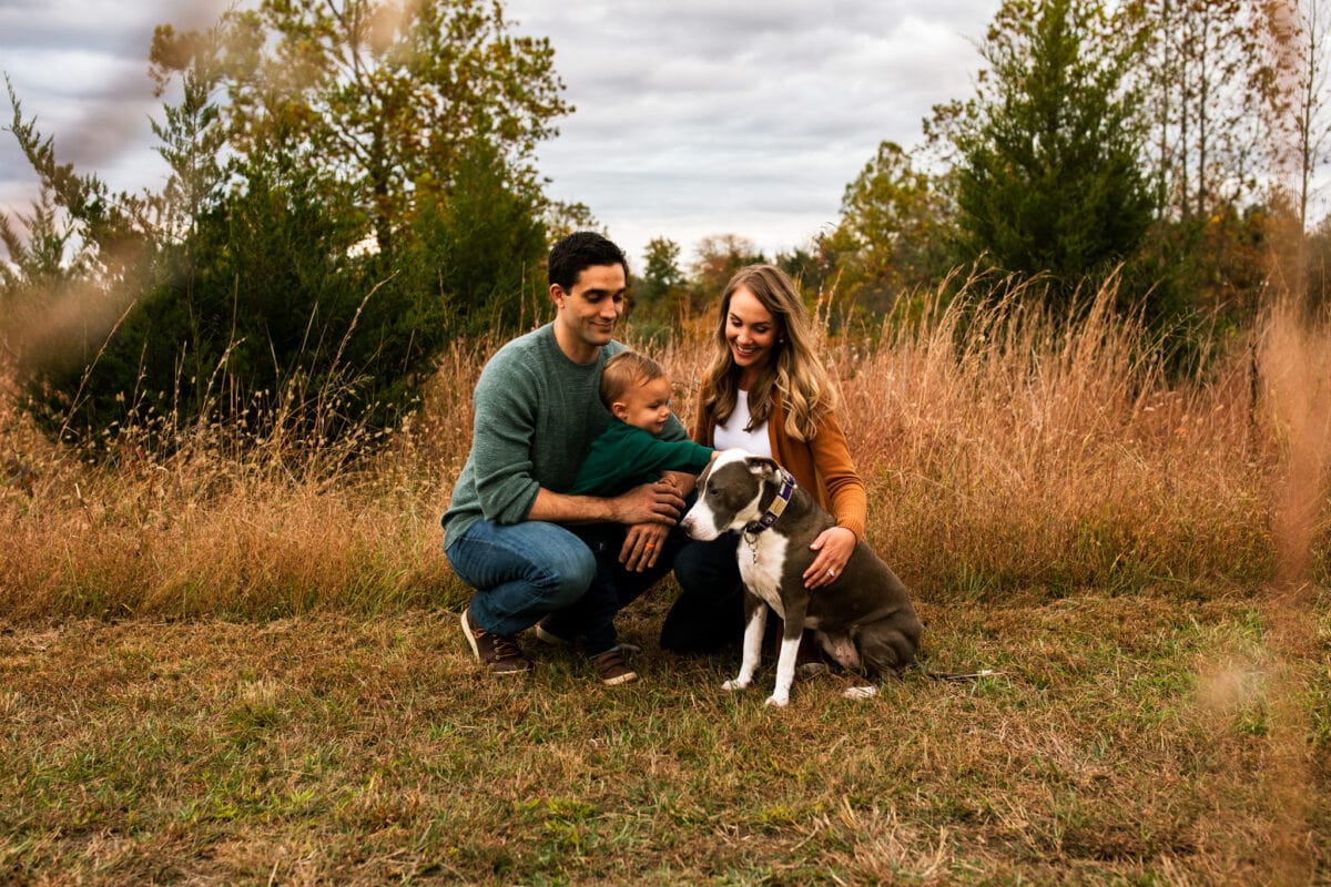 family of 3 with puppy in field of tall grass