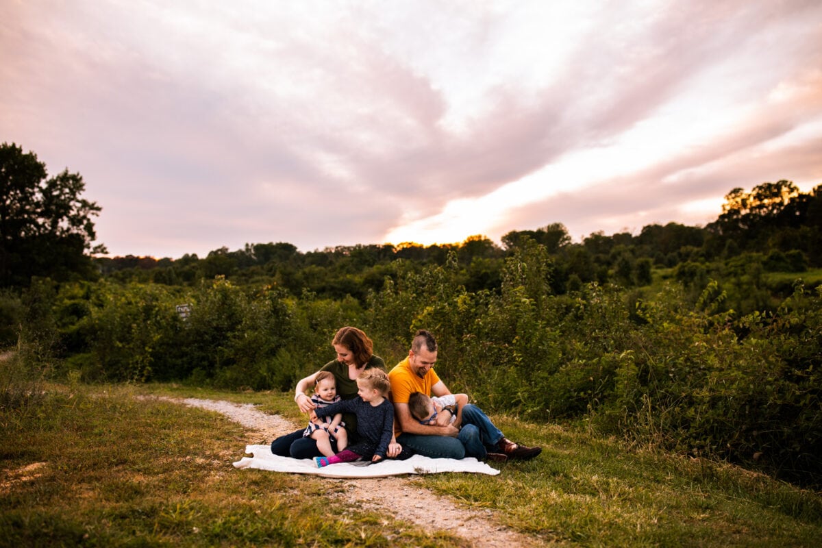 family of 5 sits on blanket under pink sky