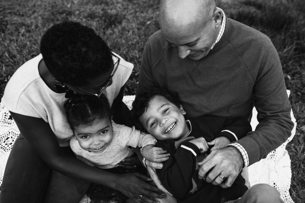family of 4 snuggling on blanket with black and white image taken from above