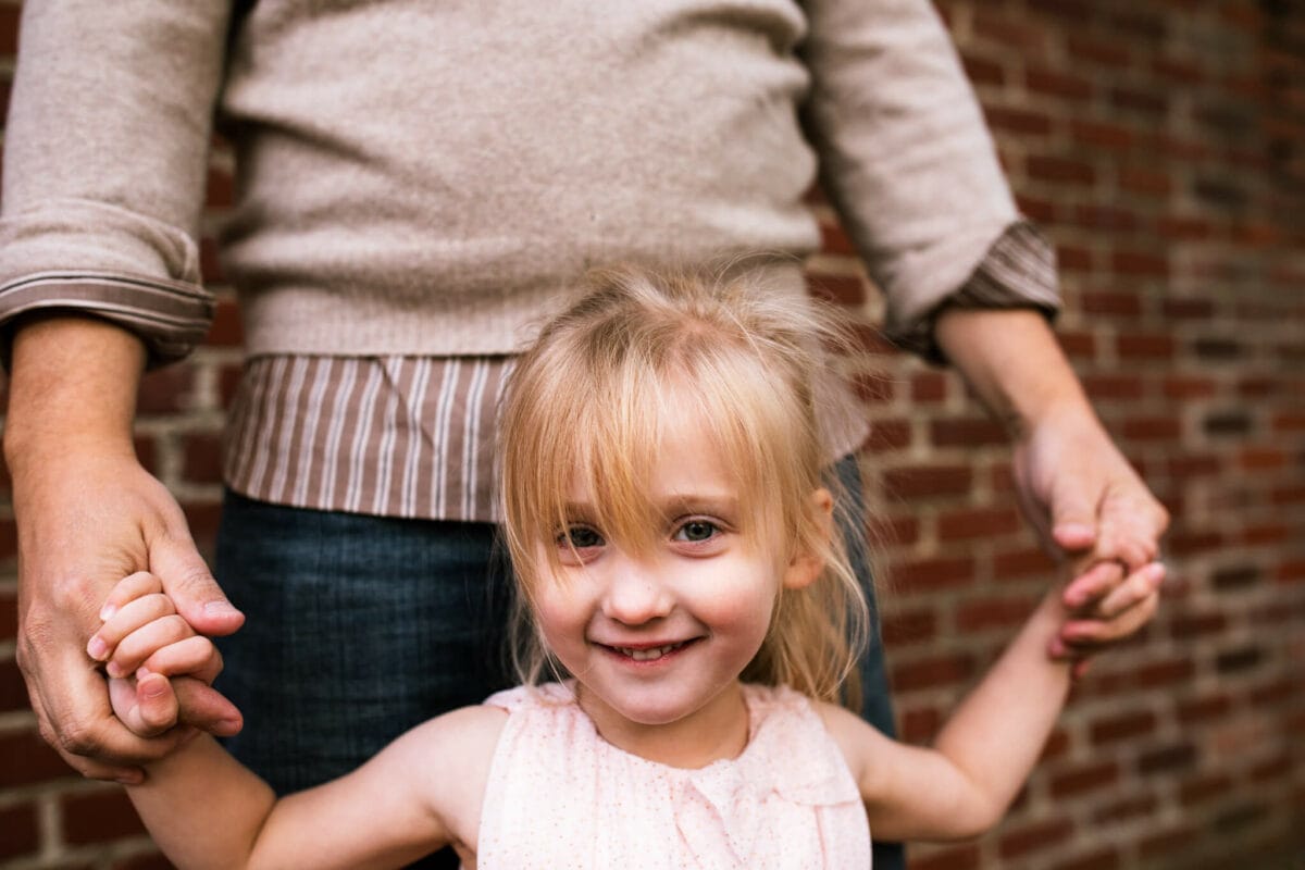 girl holds her dads hands and smiles at camera 