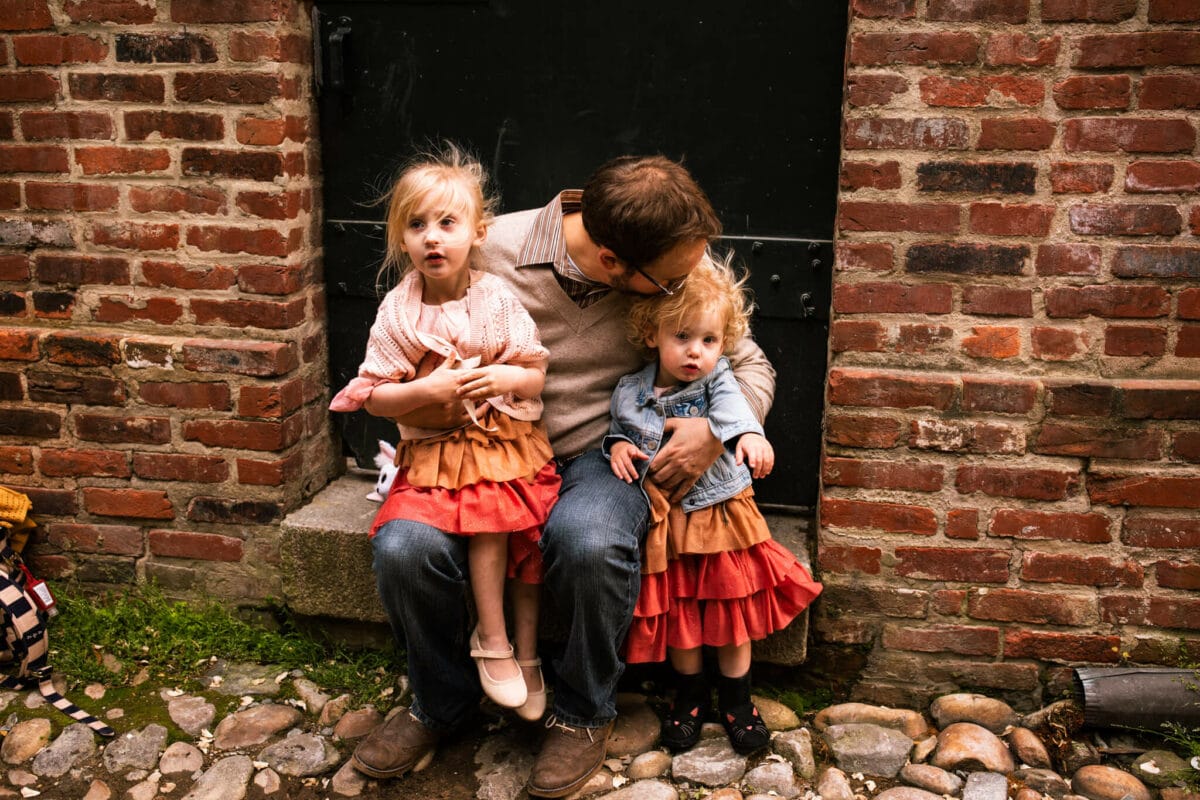 dad holds two daughters on his lap and kisses one on head the key to amazing family photos 