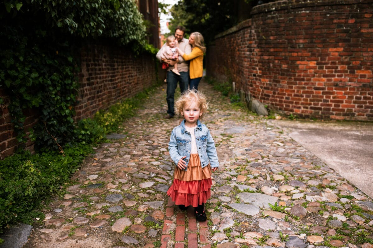 young daughter walks toward camera while family snuggles in background