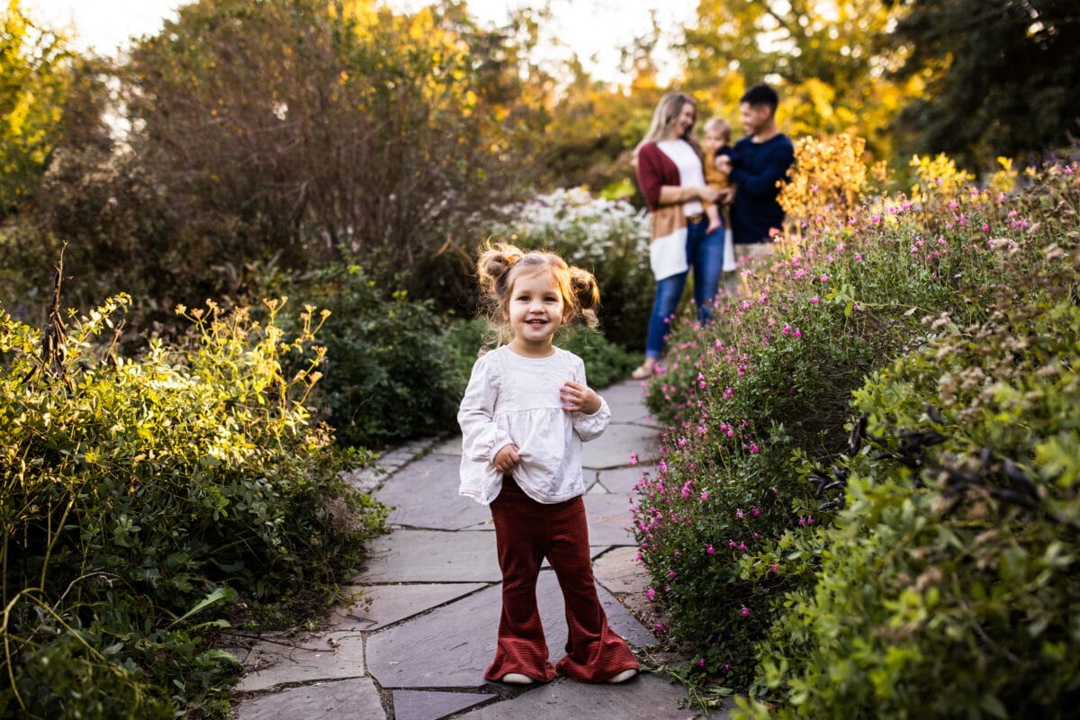 toddler girl in garden with family in background