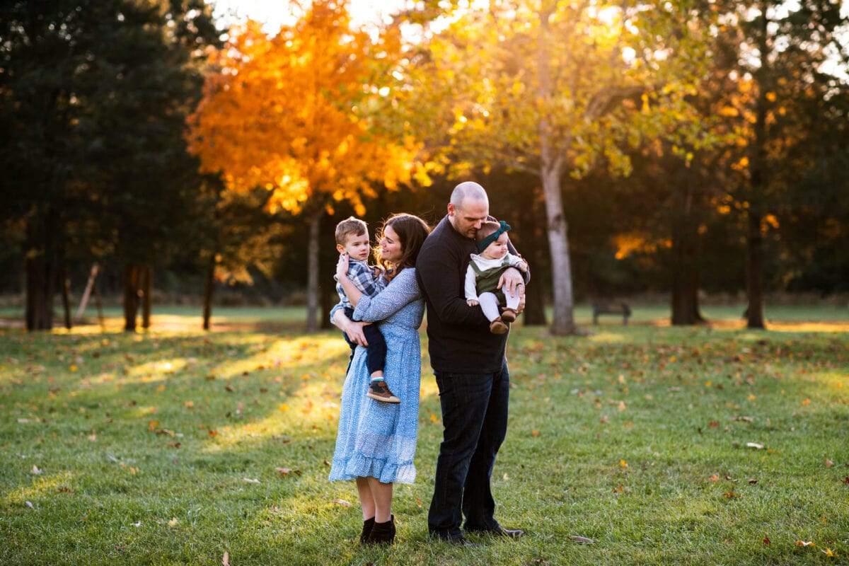 family of 4 standing together with fall leaves in background