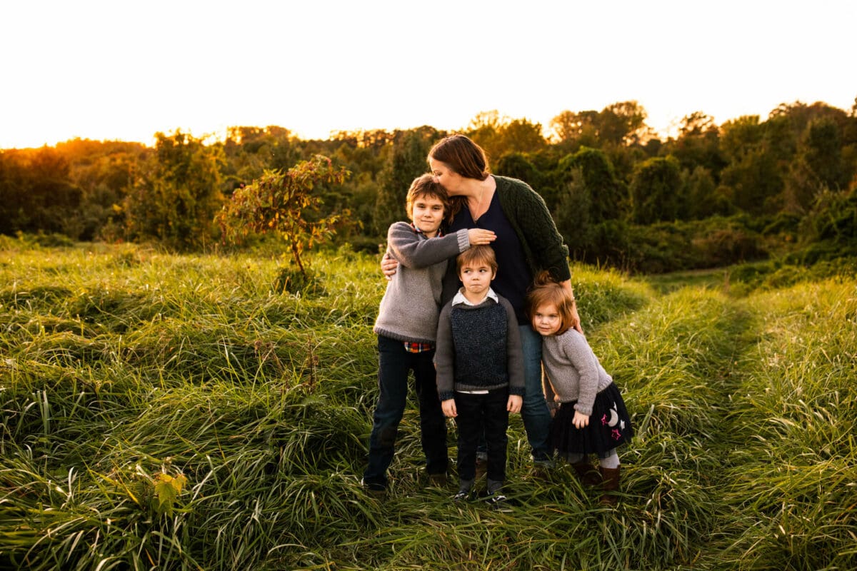 mother stands lovingly with her 3 children in open field