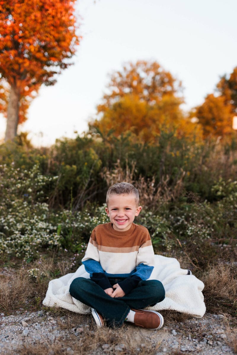young boy in sweater smiling with fall leaves