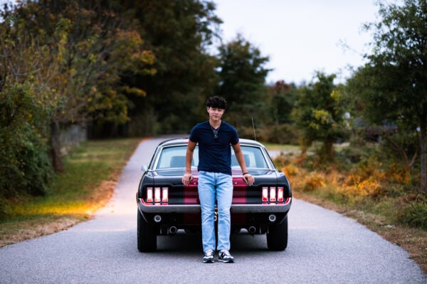 high school graduate with old car in street