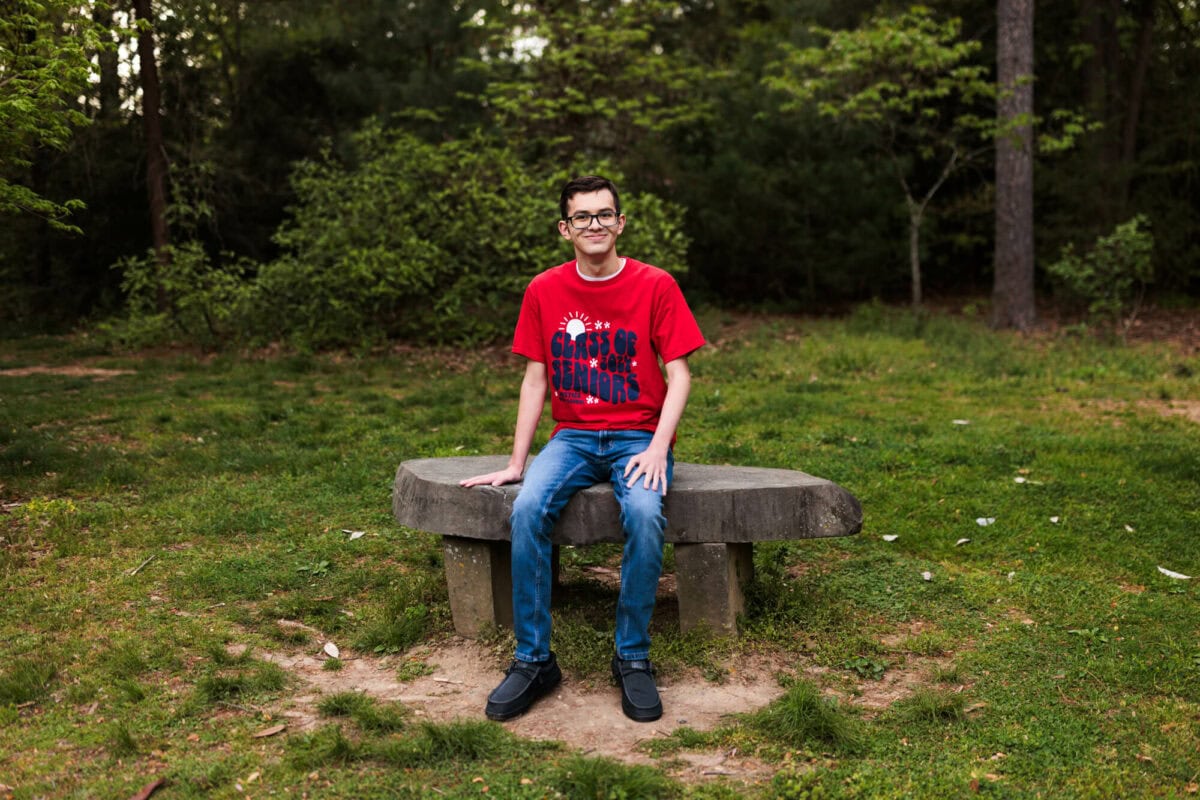 senior boy sitting on rock bench