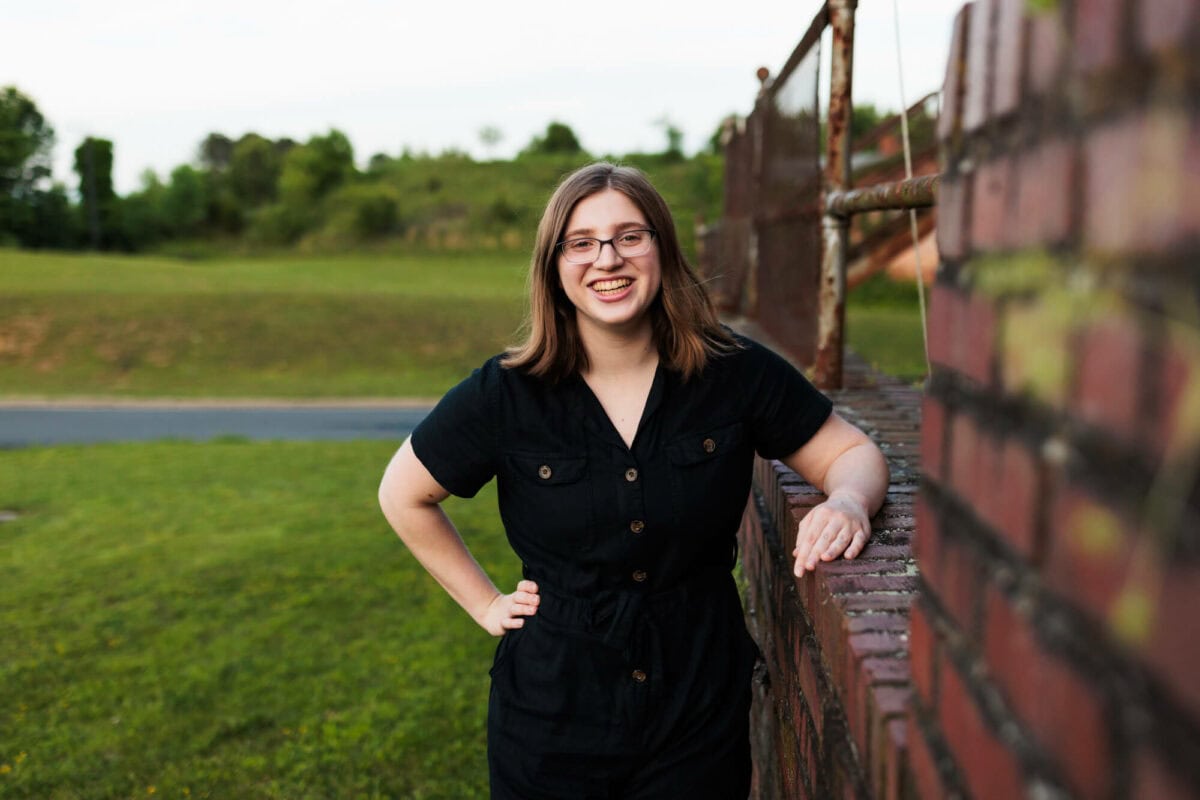 senior girl smiling with arm resting on brick wall