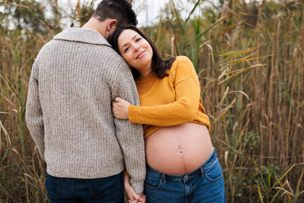 pregnant mom standing in tall grass with husband at outdoor session